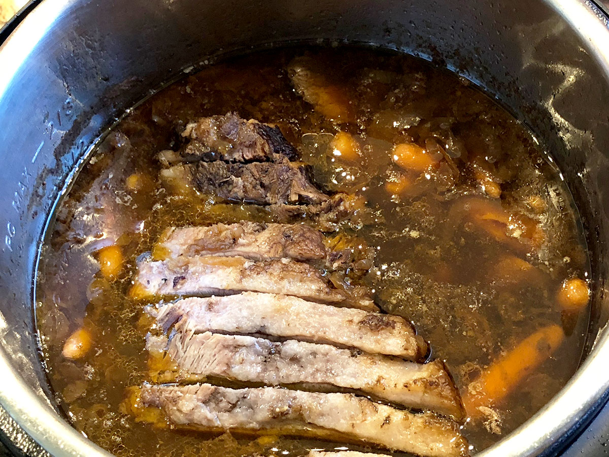 Sliced brisket placed back in the pressure cooker with carrots and potatoes.