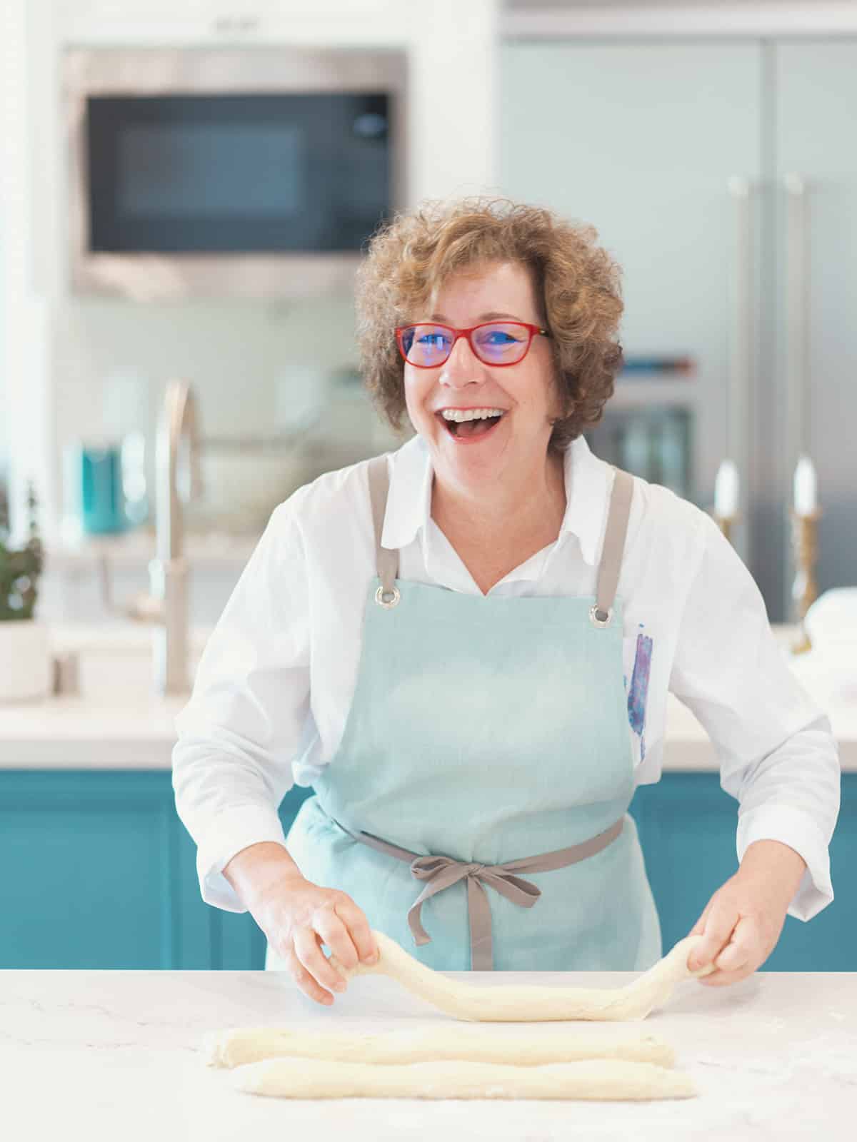 Beth Lee laughing while working with challah strands on a white counter.