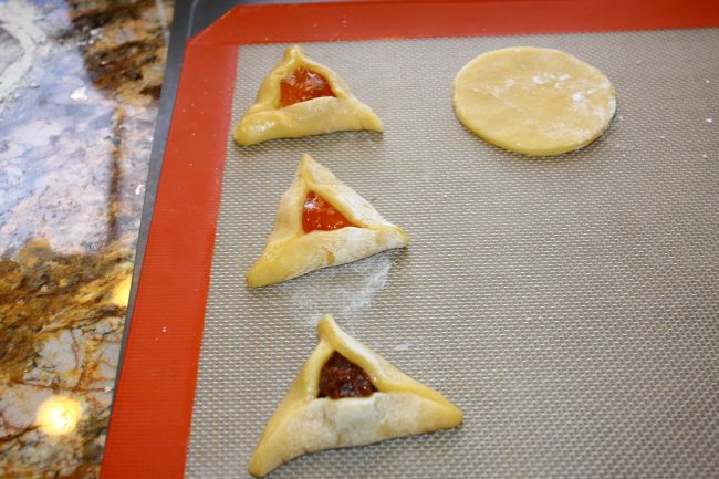 Filled dough in triangle shapes on a silpat lined pan. One piece of dough in a cirlce.