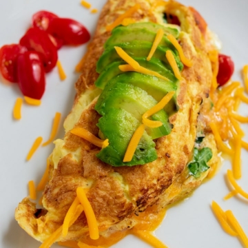 angle shot of omelet with avocado sliced on top and cherry tomatoes on the side