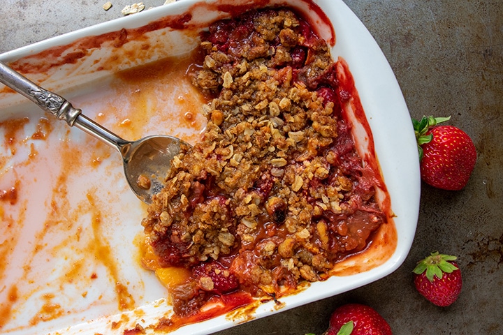 Baked fruit crisp in white rectangular pan with spoon for serving, with the majority gone, already served.
