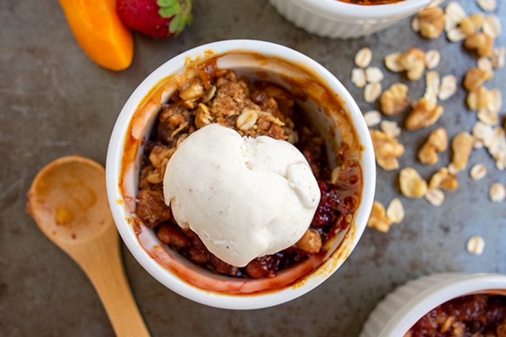 A serving of a mini fruit crisp with a scoop of vanilla ice cream on top.