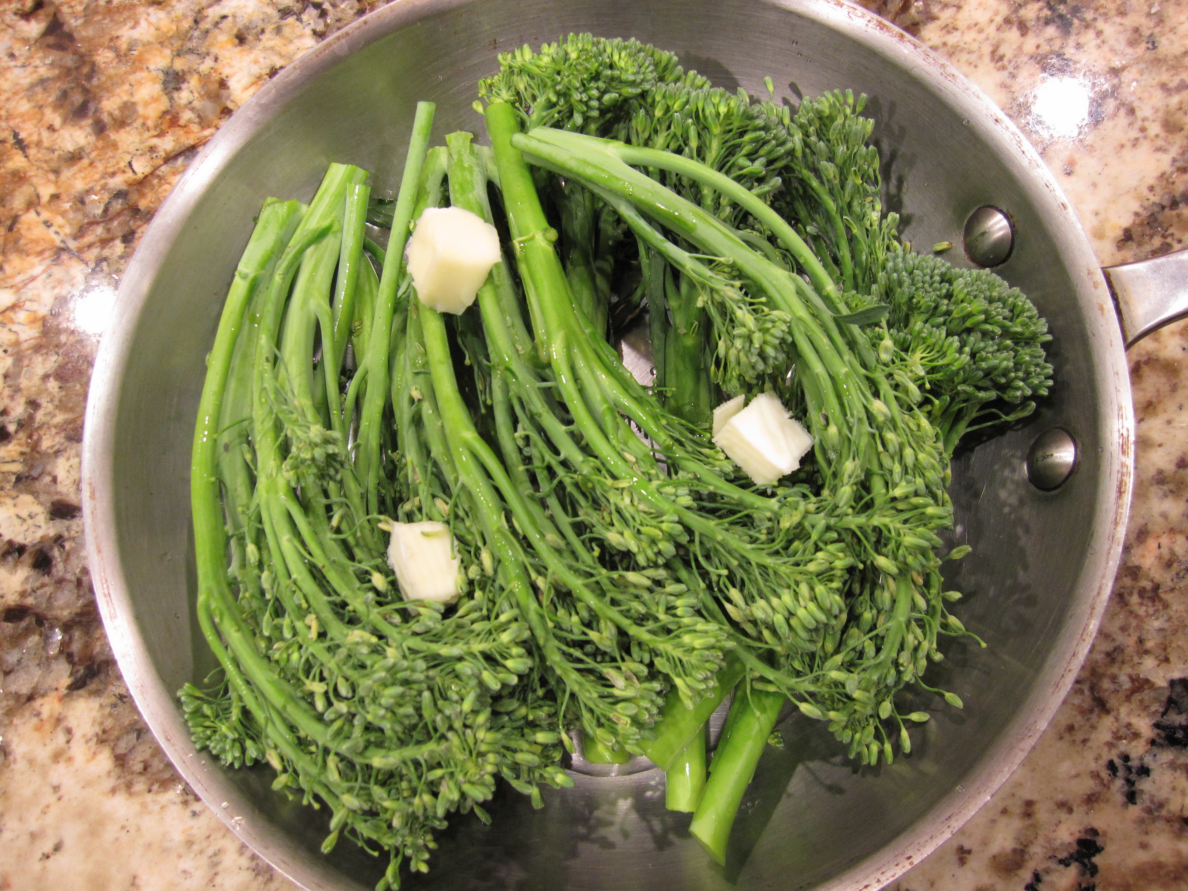 Fresh broccolini and butter cubes in 8-inch pan ready to be braised.