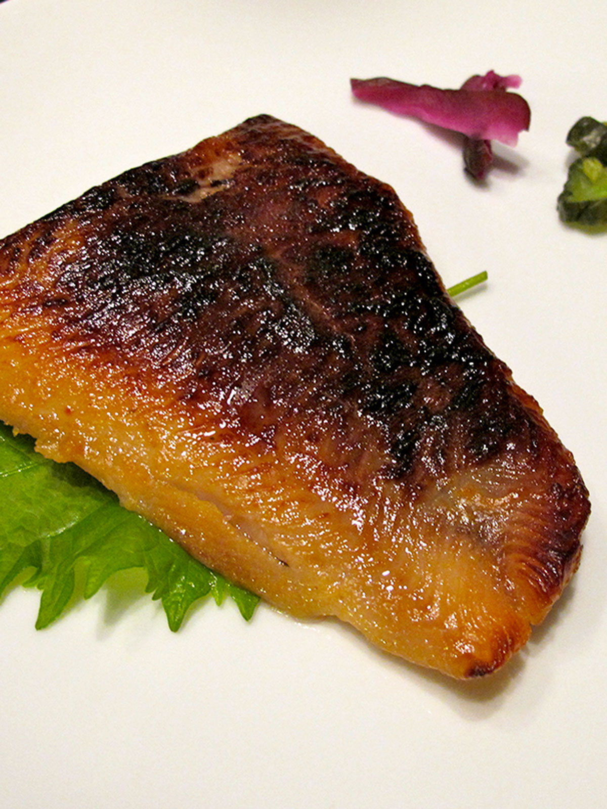 Miso marinated cod on a white plate with a shiso leaf underneath.