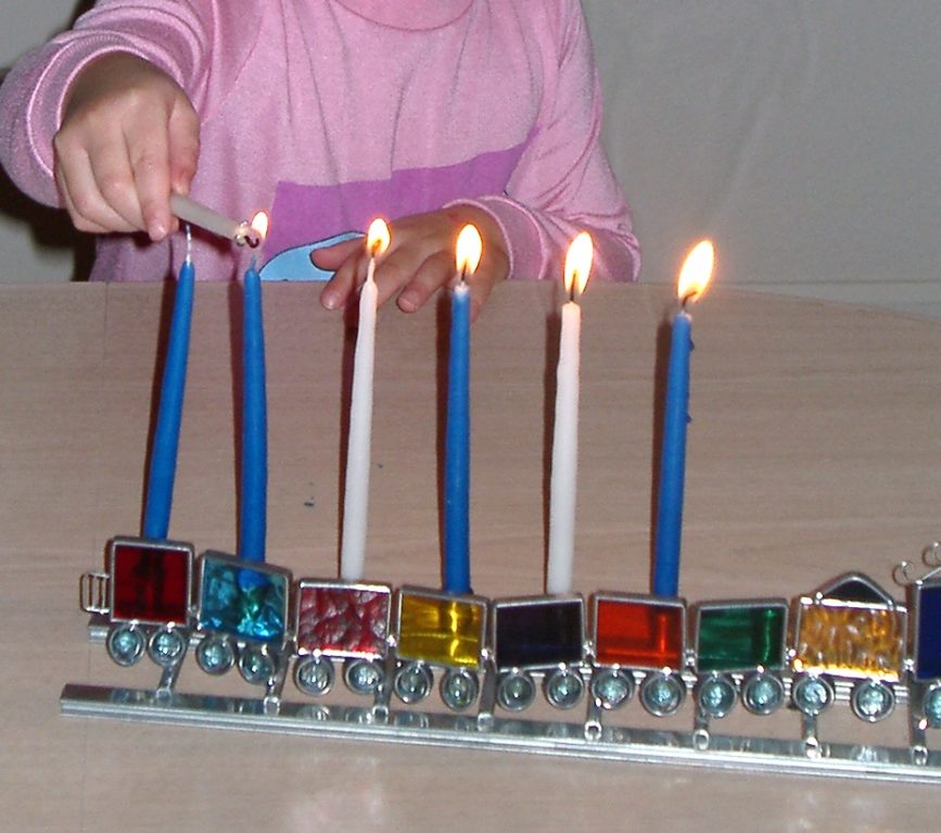 Child lighting the "hannukiah" the traditional candelabra, on the sixth night. The candle holders are in the shape of train cars made from stained glass. 