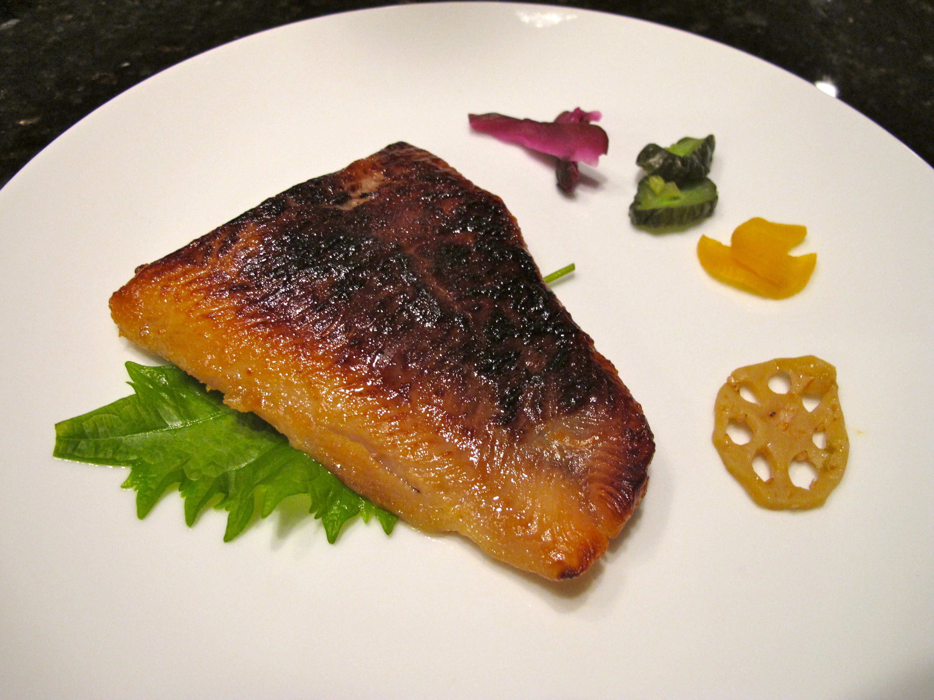 Miso marinated cod on a white plate with Japanese vegetables on the side.