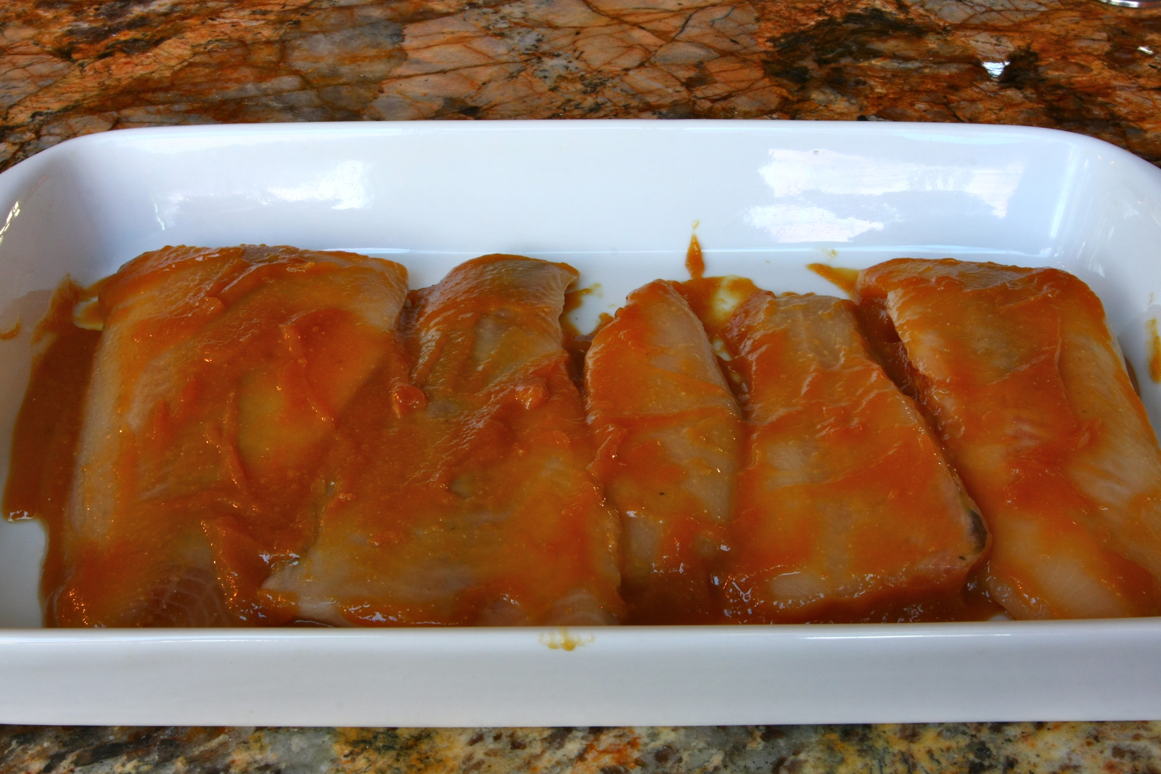 A white baking dish with cod fillets covered in the red marinade. 