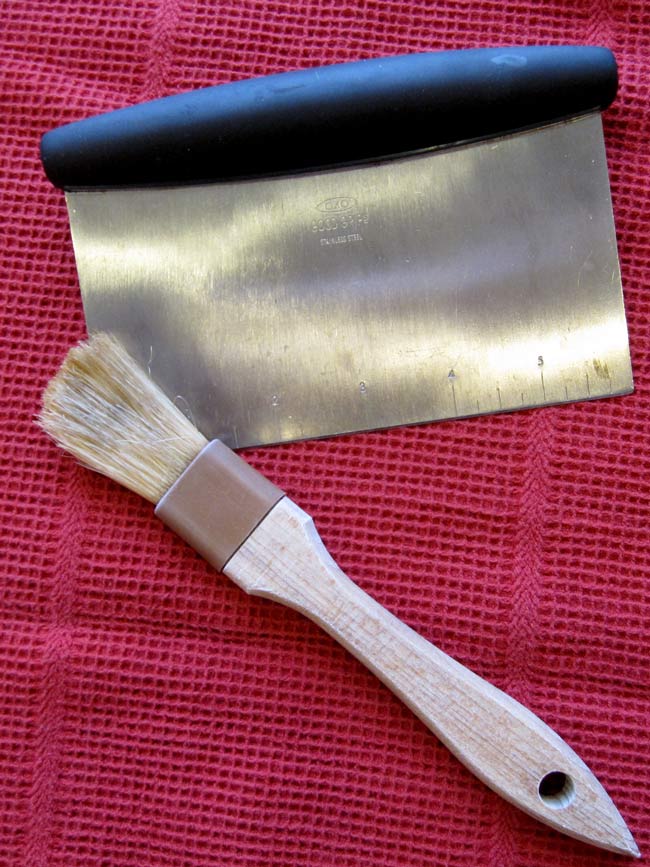 Pie dough tools - bench scraper and pastry brush on red towel.