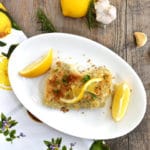 Breaded Lemon Garlic Chicken on white plate with lemon on vertical wood background