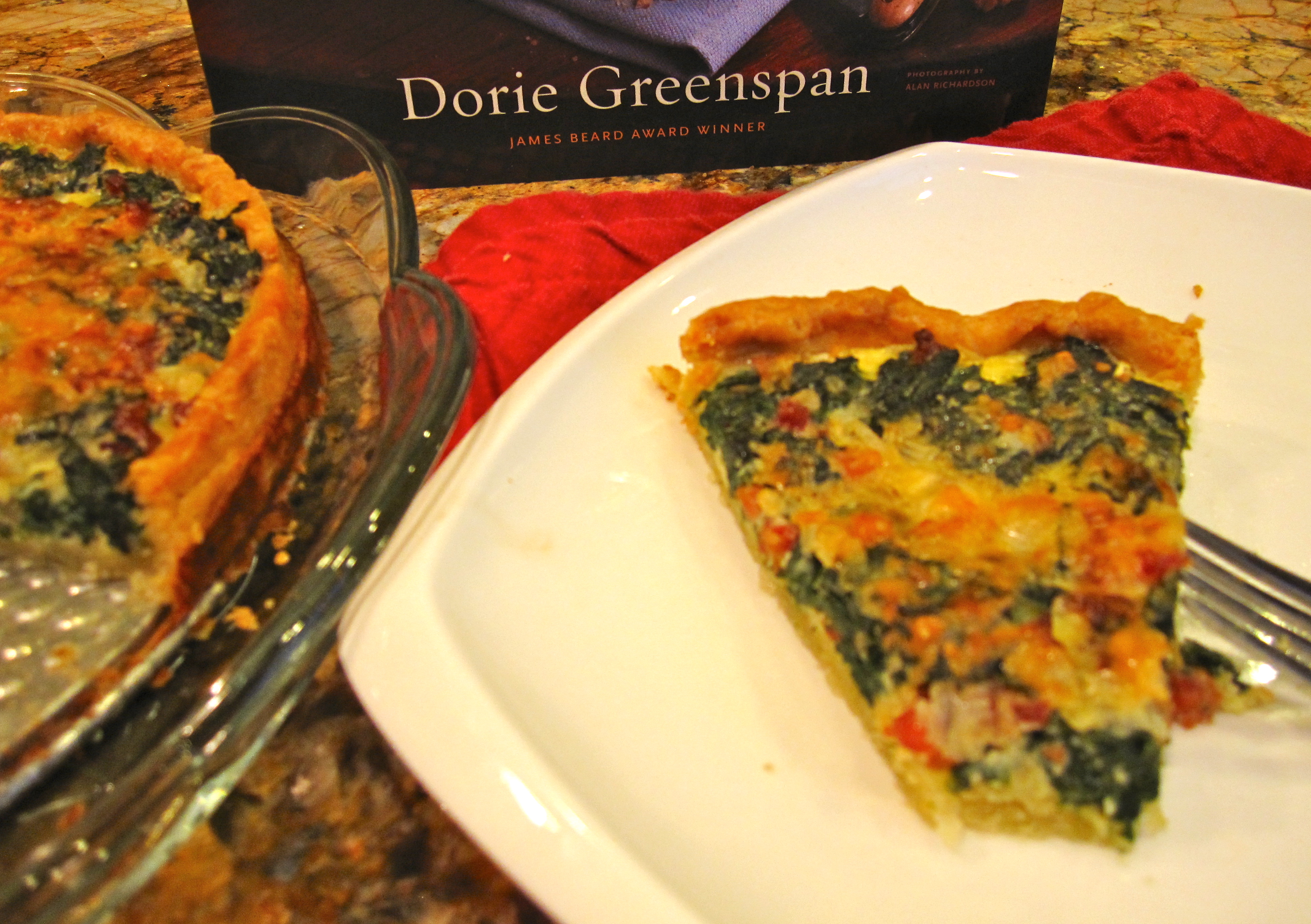 Quiche slice on white plate with fork and copy of Dorie Greenspan's Around My French Table cookbook.