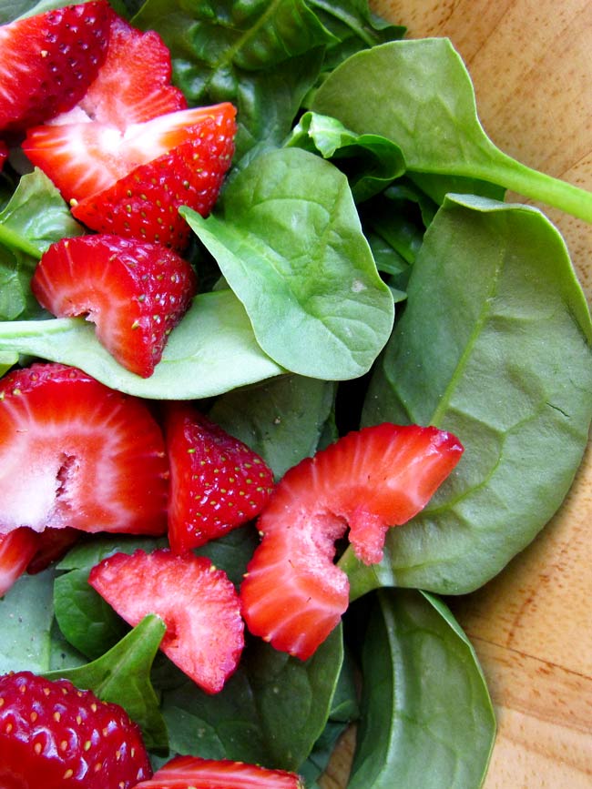 sliced strawberries and spinach in a wooden bowl