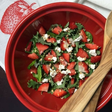 strawberry spinach salad in red bowl with wooden serving spoons