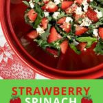 strawberry spinach salad in red bowl with serving utensils and white towel