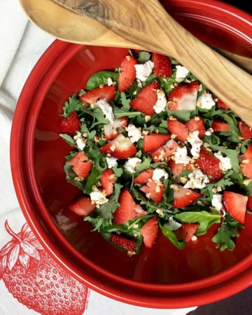 strawberry spinach salad in red bowl with serving utensils on top