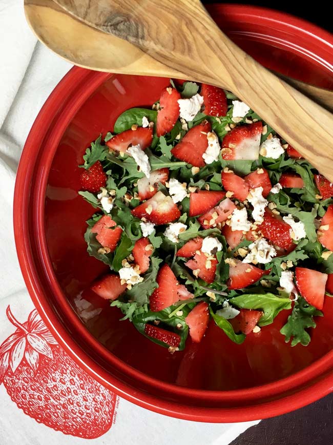 strawberry spinach salad in red bowl with serving utensils on top
