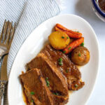 Pinterest image showing a white plate with three slices of brisket on it and some potatoes and carrots.