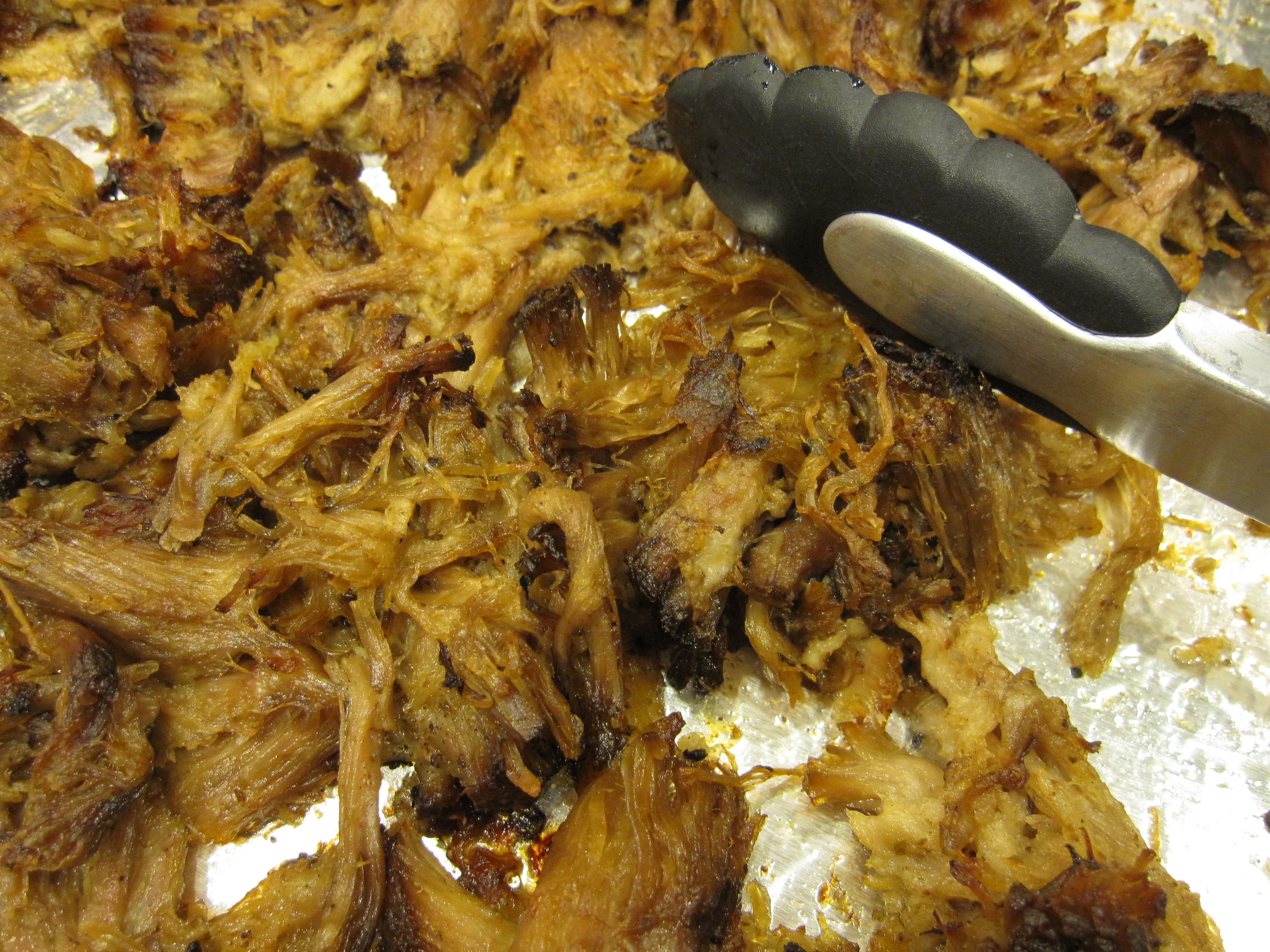Cooked carnitas being stirred with tongs.