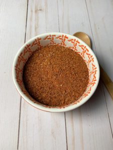 spice rub in orange bowl with wooden spoon on wood background