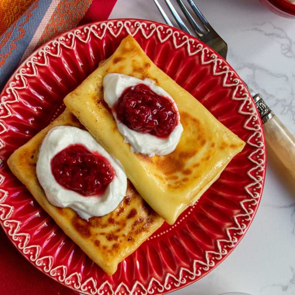 2 blintzes on red plate topped with sour cream and jam