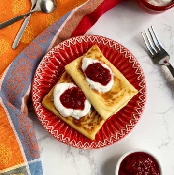 two blintzes on red plate with strawberry jam and sour cream