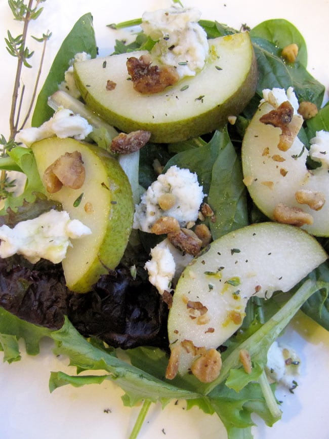 arugula and pear salad with toasted walnuts on white plate