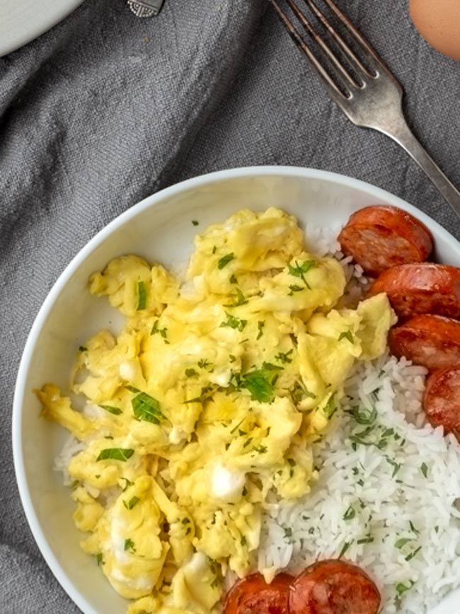 A serving of soy sauce eggs, rice and Portuguese sausage on white plate and grey tablecloth.