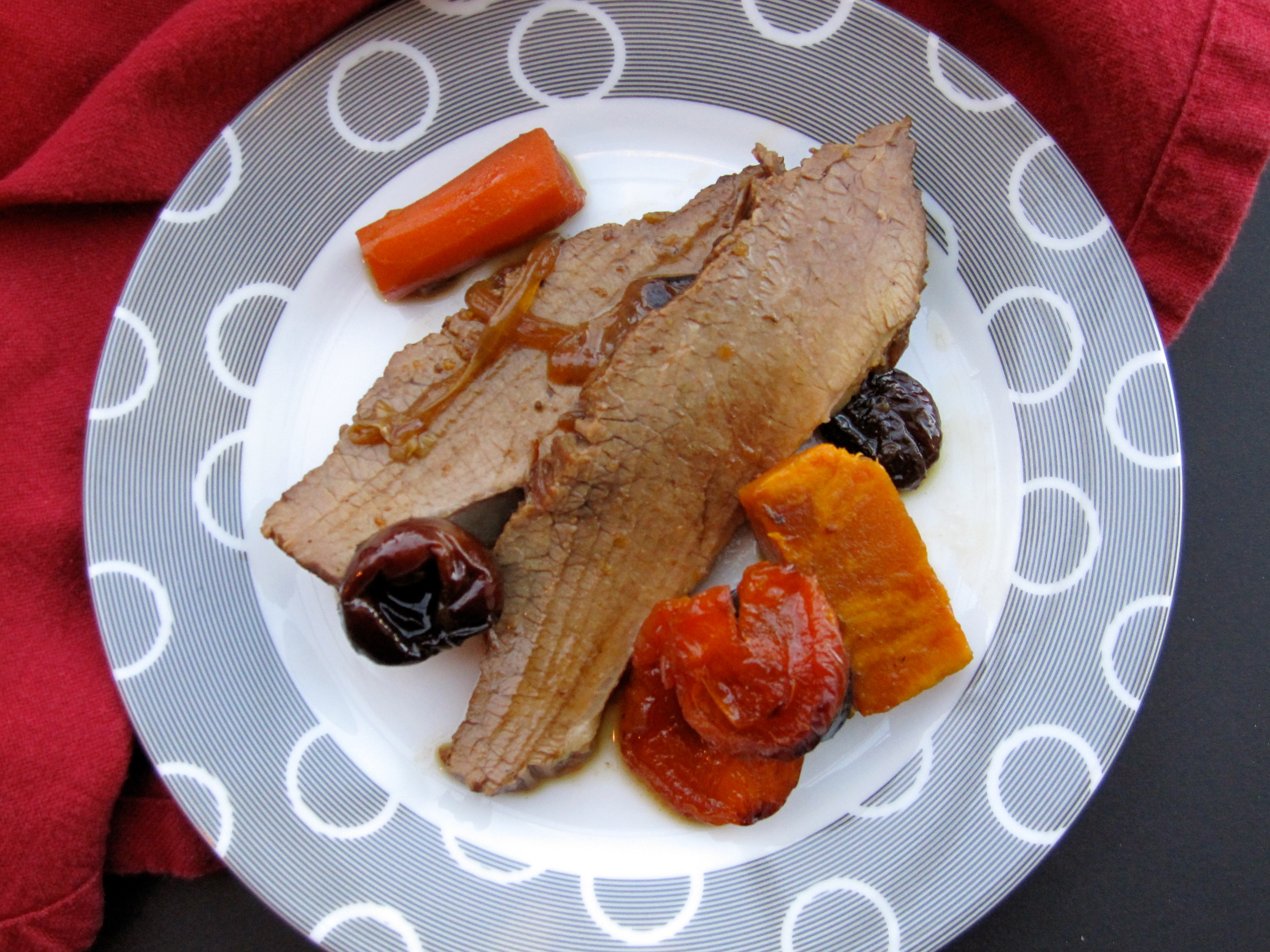 Grandma Ethel's Tzimmes style brisket on a white plate with grey circles on border.