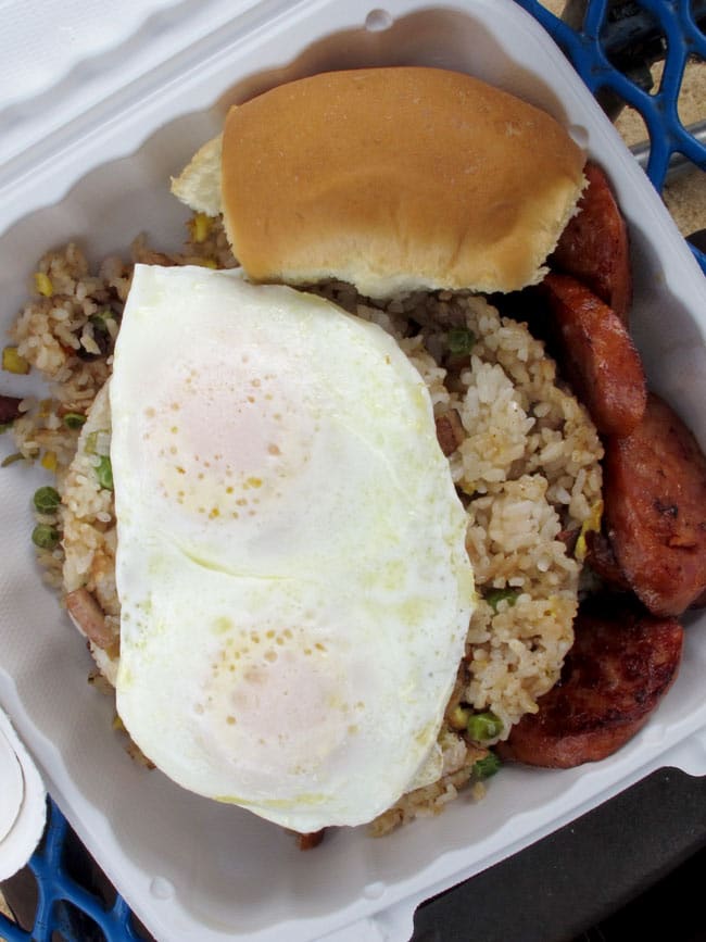 A white take out container of fried rice over easy eggs and Portuguese sausage from Ted's Bakery.