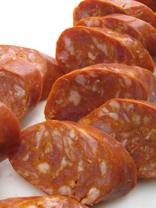 Close up of sliced sausage on white cutting board.