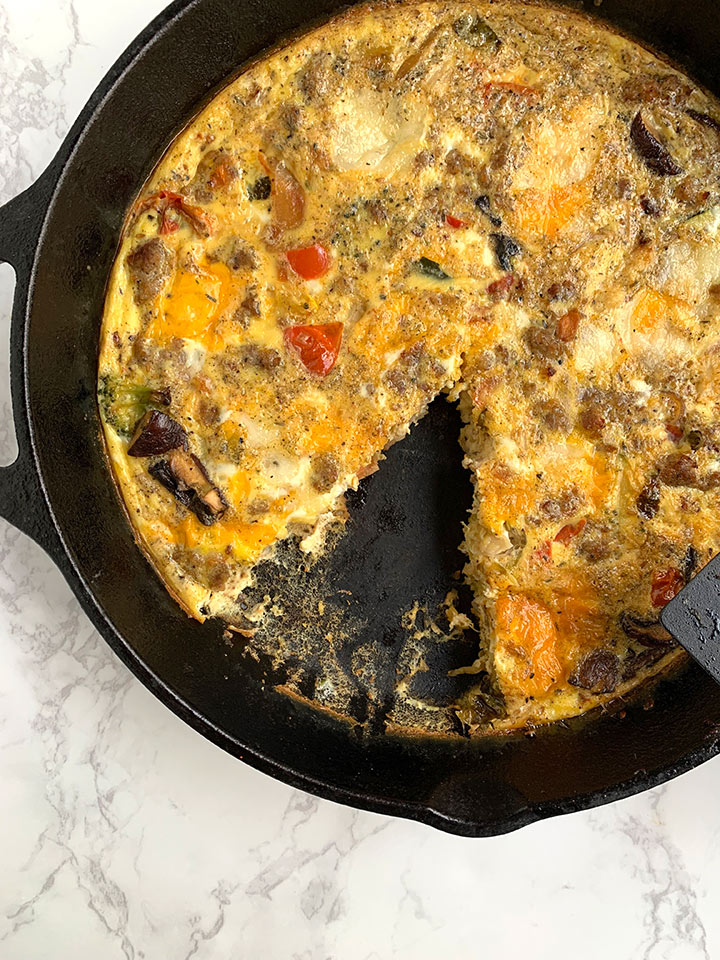 Frittata in a cast iron pan on marble counter, with one slice missing.