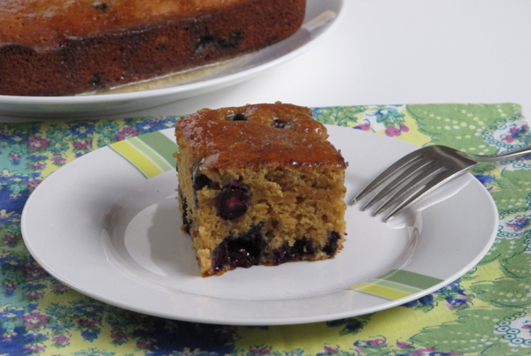 A square serving of Melissa Clark's maple blueberry tea cake on a white plate with a fork.