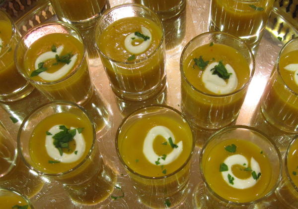 Squash soup in clear shot glasses on a metal tray.