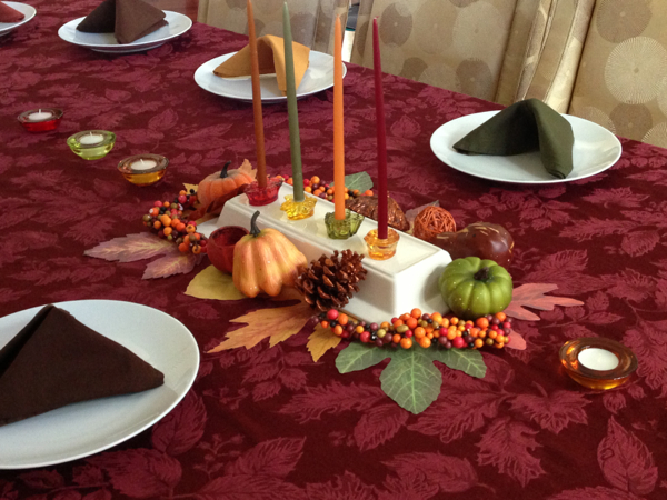 Decorated Thanksgiving table set with pumpkins, pine cones, and fall leaf decorations.
