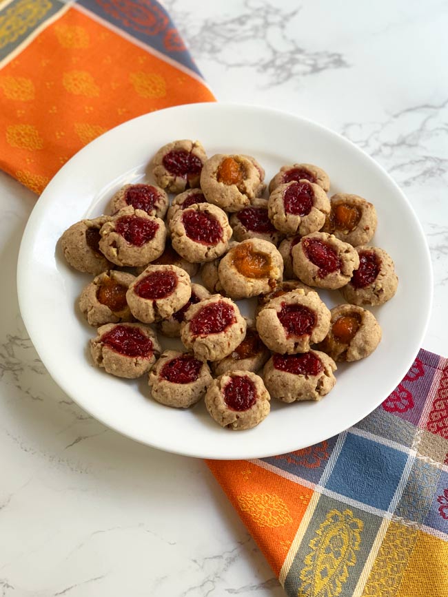 Jam thumbprint cookies on white plate with multi-colored napkin.