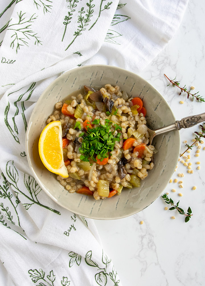Mushroom barley soup in gray bowl with lemon on marble background.
