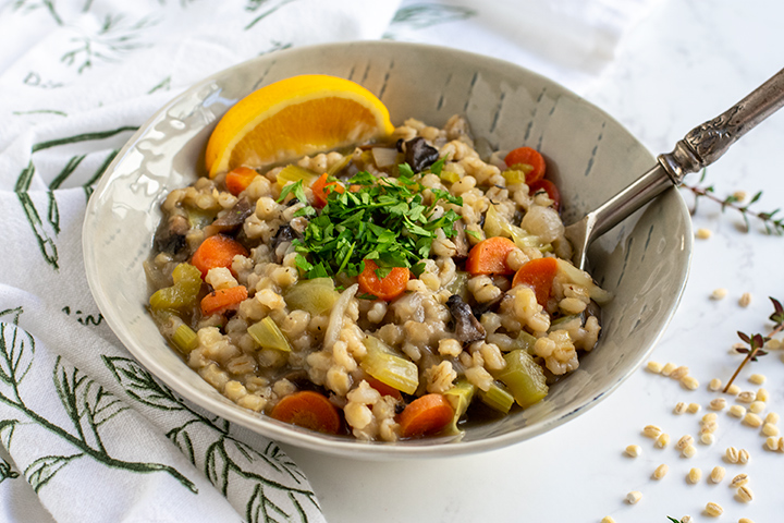 Barley risotto soup in gray bowl with lemon wedge and metal spoon.