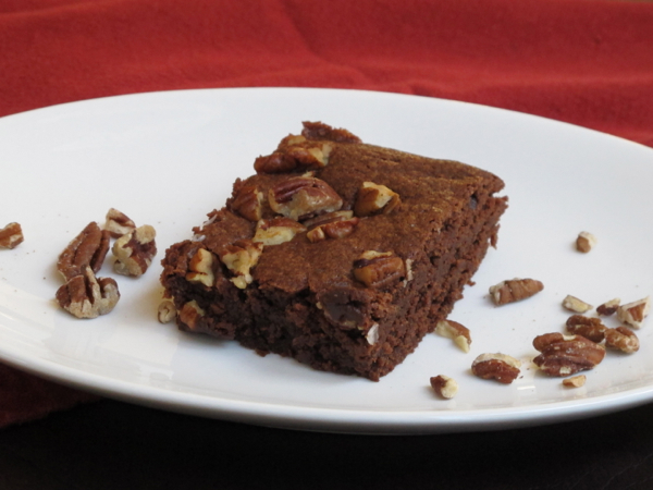 A single mocha brownie with toasted pecans and sea salt on a white plate.