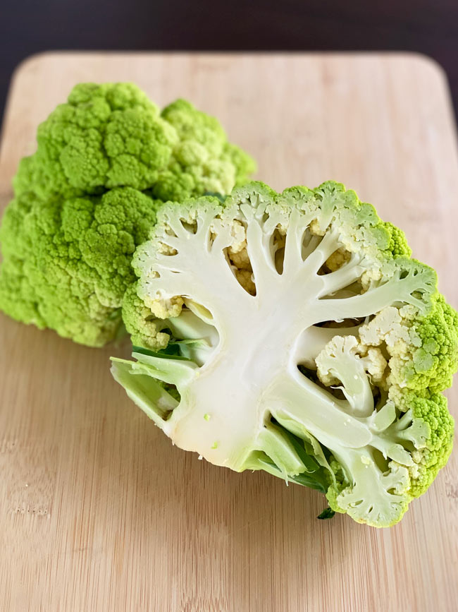 Whole green cauliflower cut in half on cutting board.