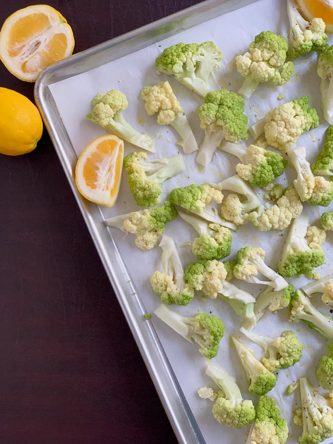 Green cauliflower florets with lemons on parchment lined baking sheet.