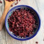 close up of barberries in blue bowl with wooden spoon nearby