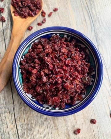 close up of barberries in blue bowl with wooden spoon nearby