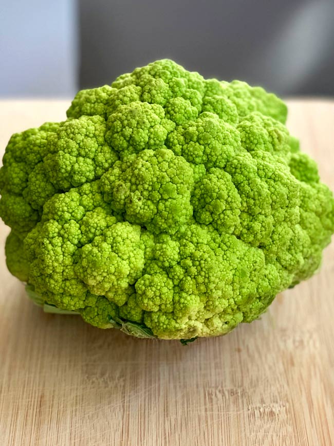 A whole head of green cauliflower on bamboo cutting board.