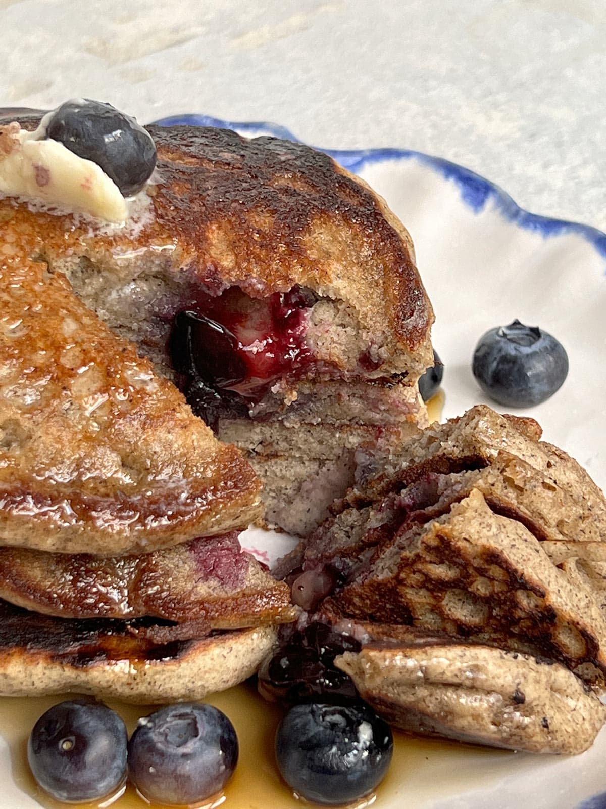 Stack of buckwheat pancakes on a blue-rimmed plate with blueberries and syrup.