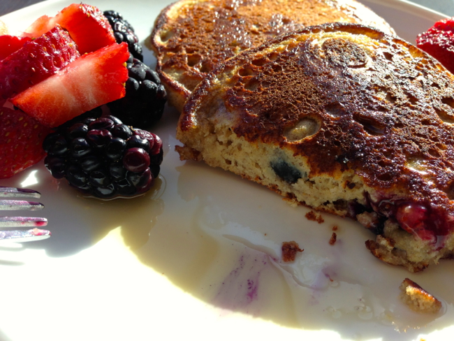 Close up of a plate of perfect pancake cut in half to show fluffy interior along with some syrup on the plate. Some fresh berries are the garnish.