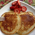 Two pancakes on a white plate with sliced strawberries.