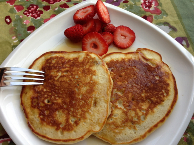 A plate of perfect pancake recipe pancakes with syrup poured on top and fresh strawberries on the side. 