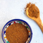 Baharat in a blue bowl with wooden spoon in a pinterest image.