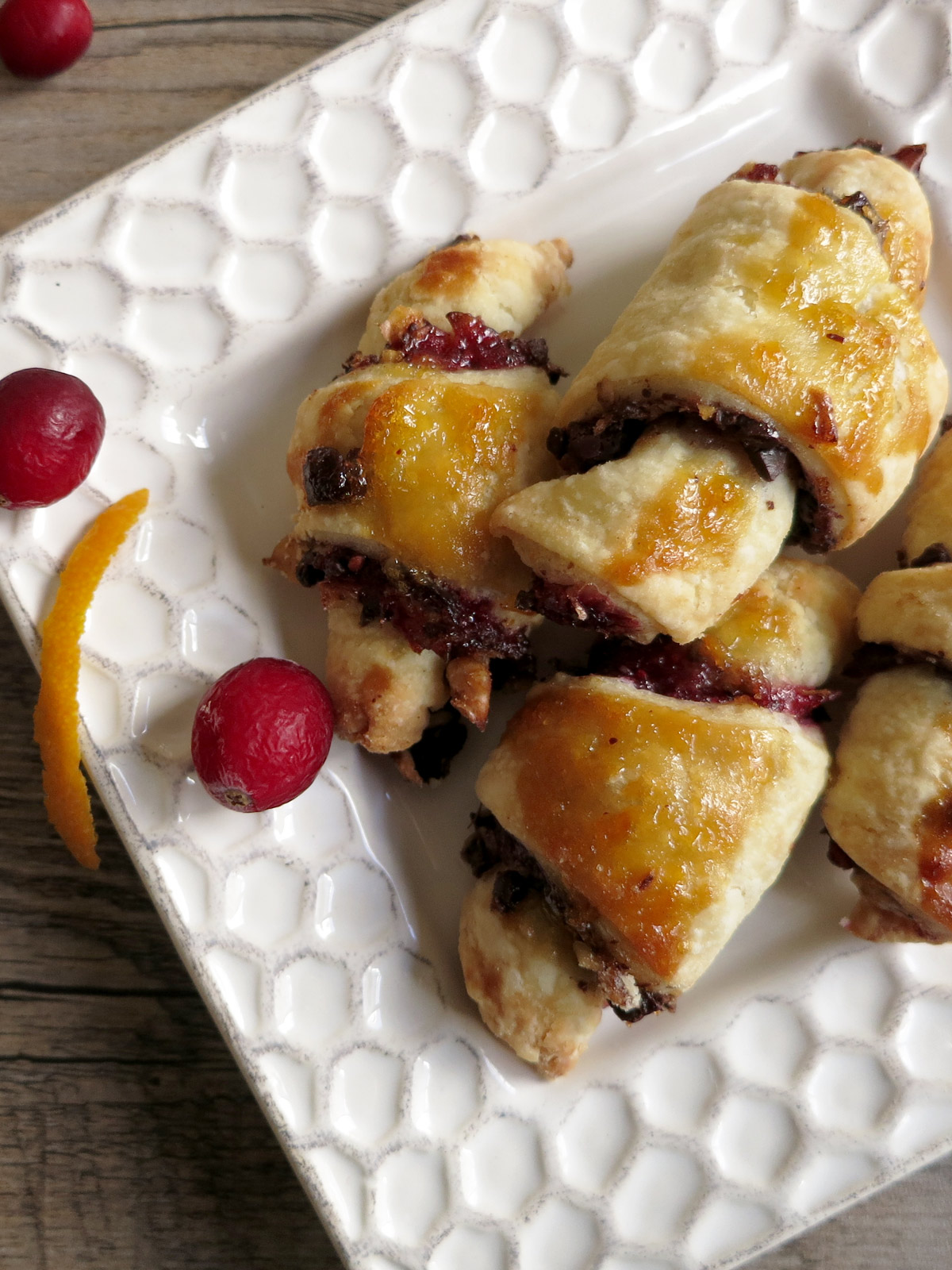 Cranberry orange rugelach on a white plate decorated with fresh cranberries and orange peel.
