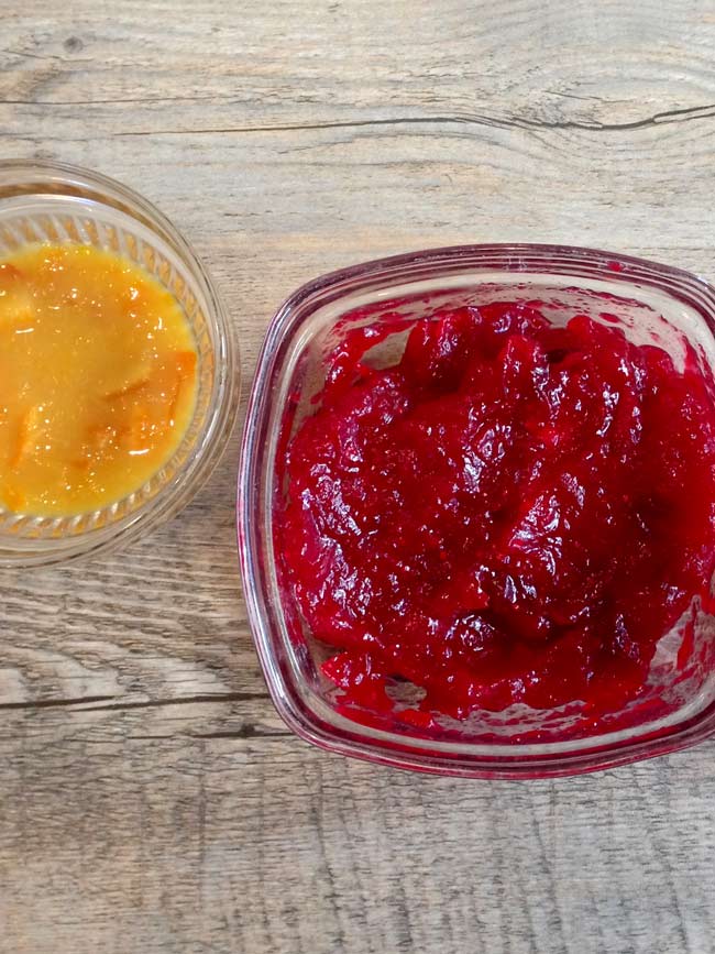 Small clear glass bowls of cranberry jam and orange marmalade.