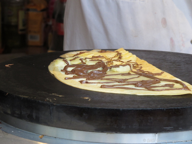 A crepe cooking with chocolate drizzled over it.